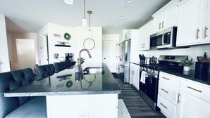 Une cuisine moderne avec des meubles blancs, des appareils en acier inoxydable et un îlot central doté d’un plan de travail noir.