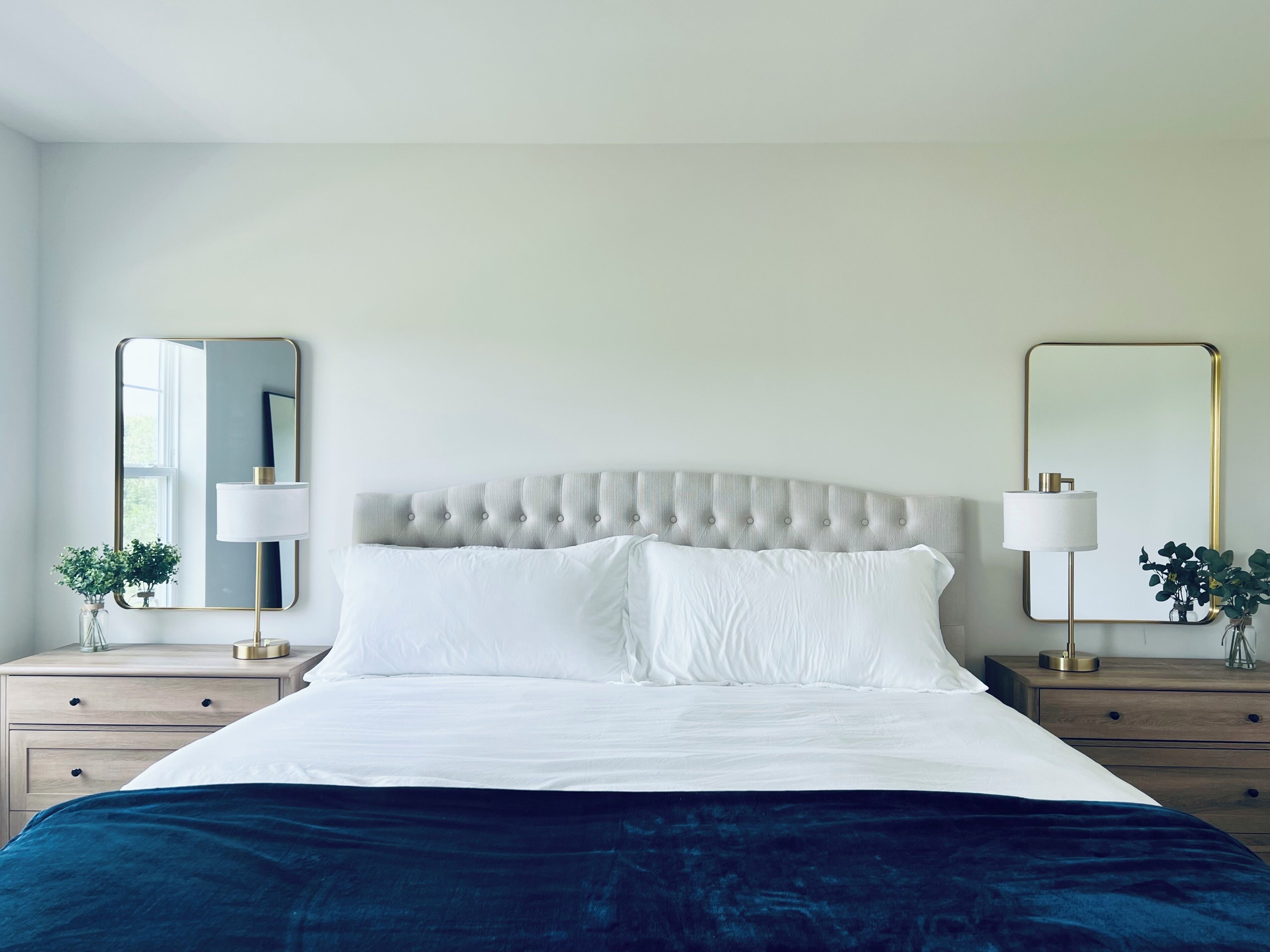 A neatly made bed with a tufted headboard, two bedside tables with lamps, and two wall mirrors.