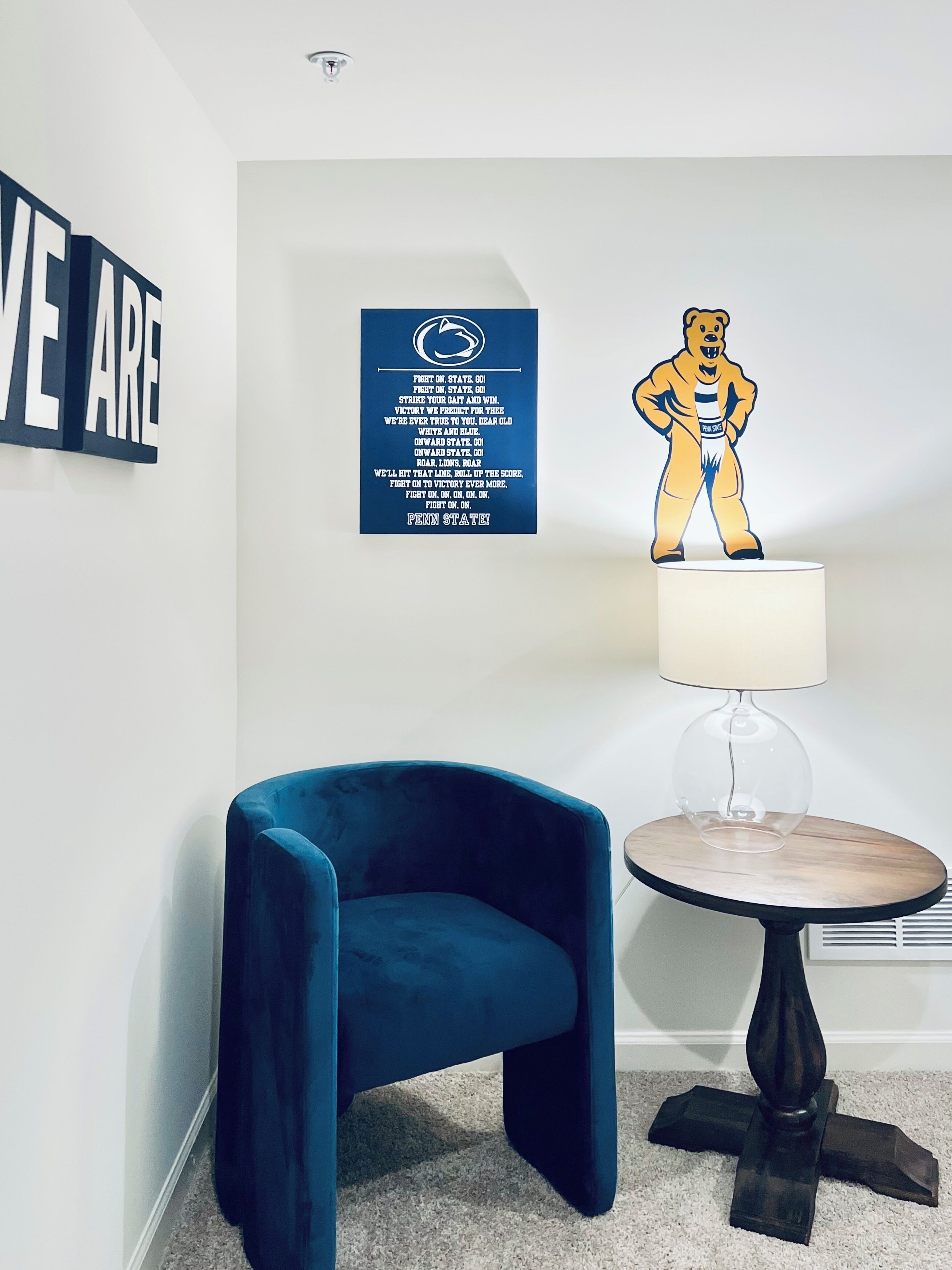Een kamer met een blauwe velours stoel, een tafel met een lamp, en een muur met een motiverende poster en een illustratie van een beer.