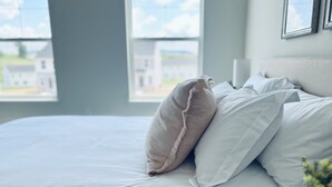 Un lit bien fait, avec une literie blanche et un seul oreiller beige.