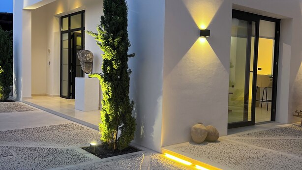 A modern building with a white exterior, a stone planter with plants, and a well-lit entrance.
