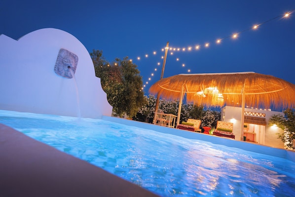 A pool area with a thatched-roof structure and string lights.