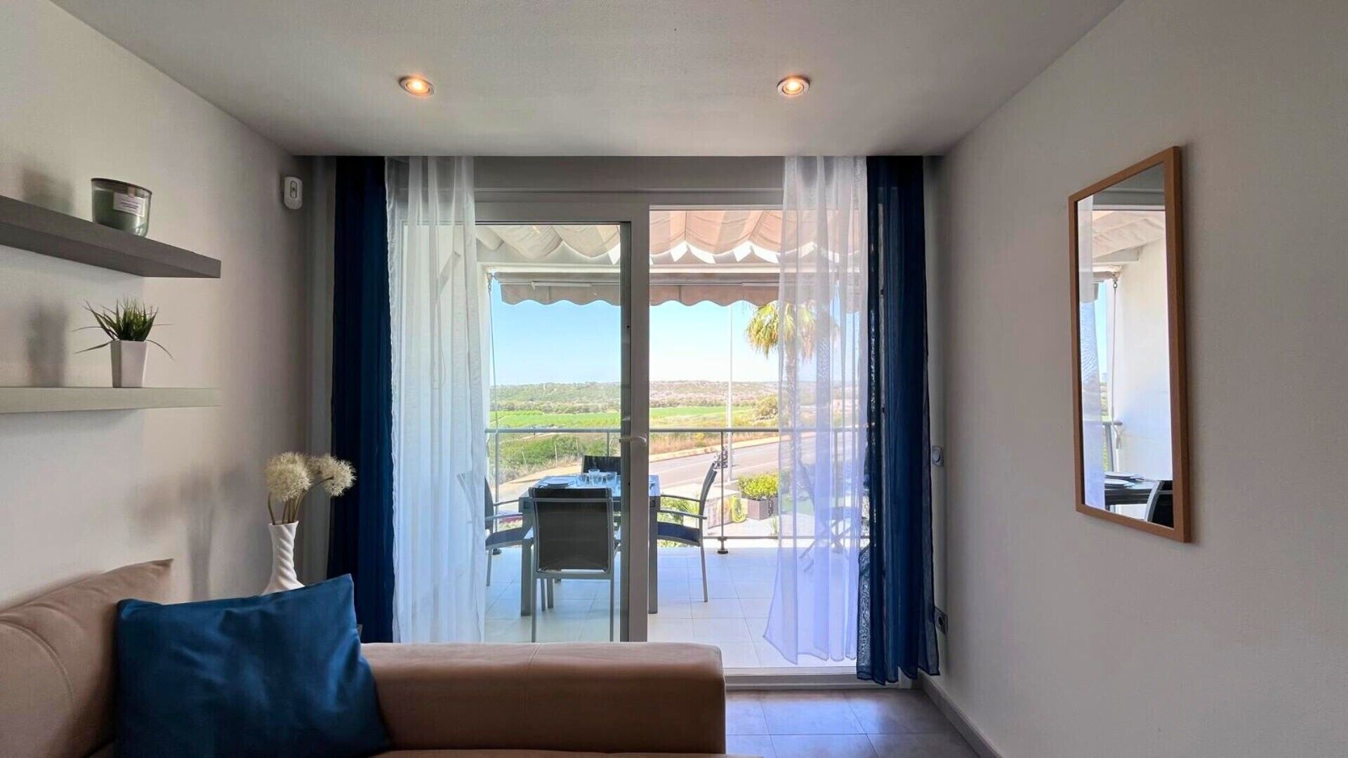 Un soggiorno con divano, un tavolo da pranzo con sedie, un balcone vista campagna e un grande specchio a parete.