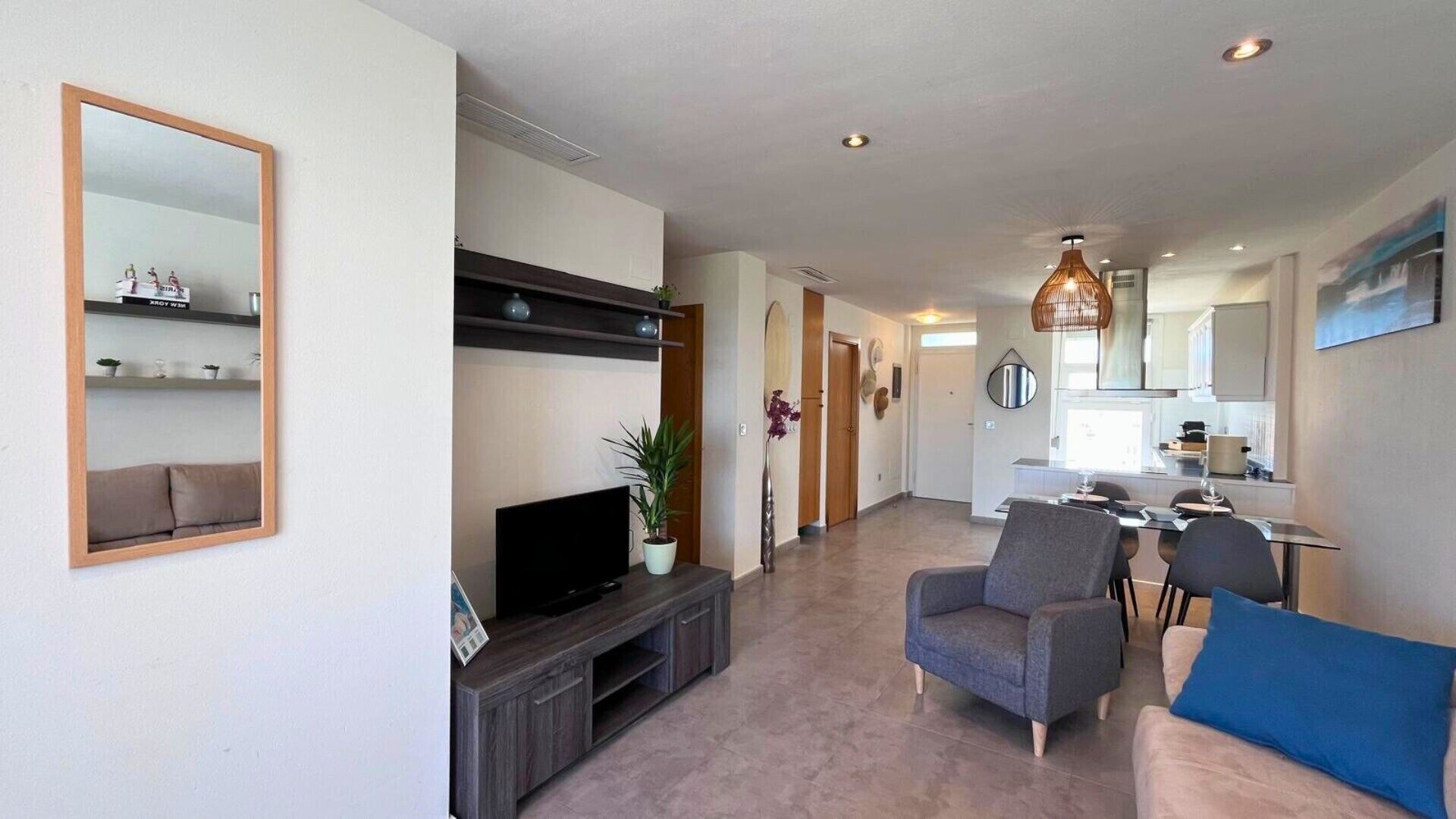 Una sala moderna con televisión, sofá y sillón, que da a una cocina y zona de comedor.