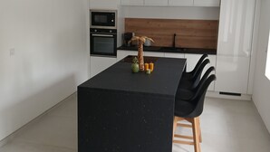 Moderni keittiö, jossa on keskellä sijaitseva saareke, musta työtaso ja puiset jakkarat.