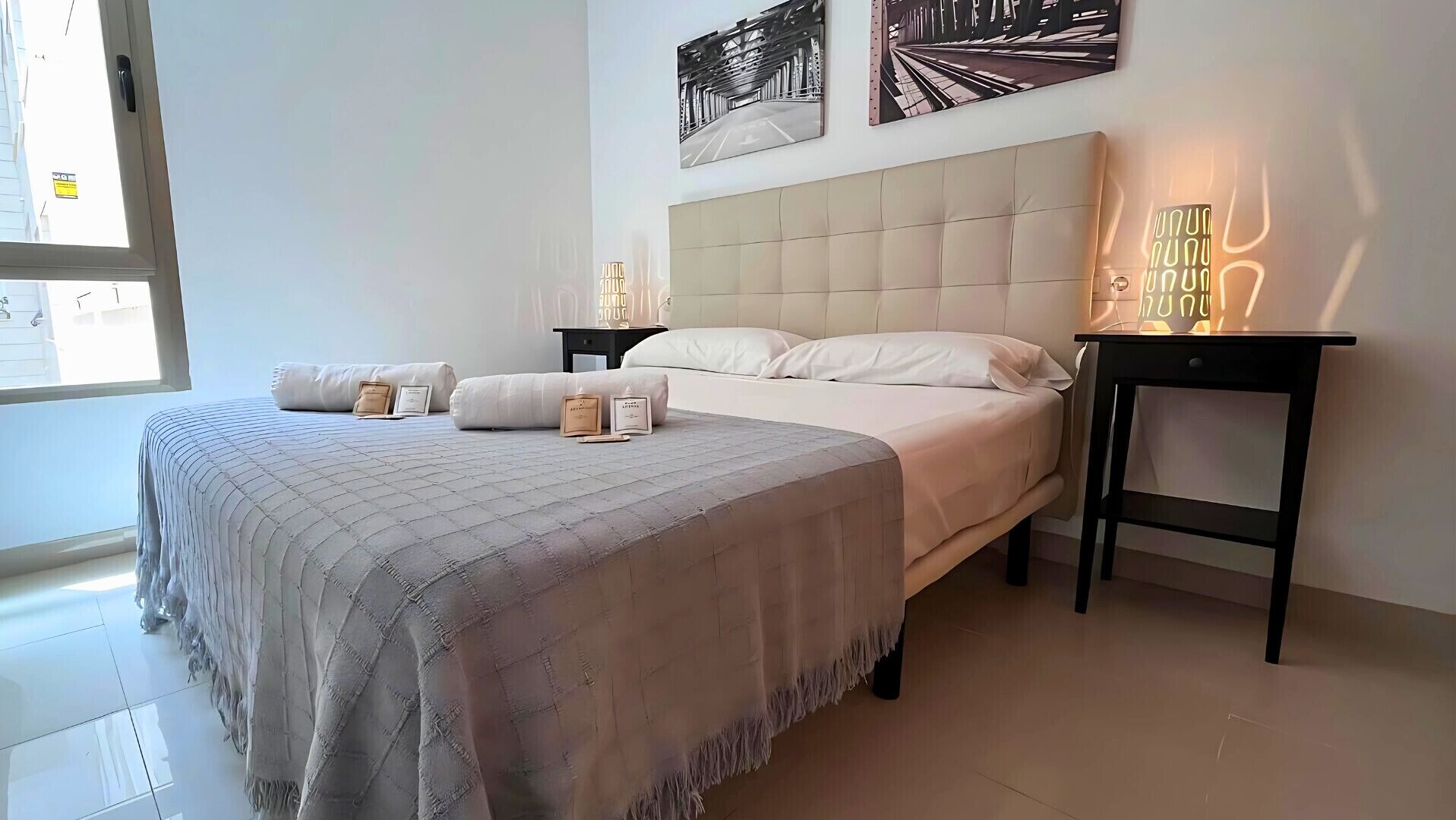 Un dormitorio con una cama grande, dos mesitas de noche, un ventanal y obras de arte en las paredes.