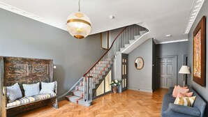 A spacious living area with a herringbone wood floor, a staircase with a wooden handrail, a grey sofa with patterned cushions, and a round mirror on the wall. - Chequer -  a holiday let that sleeps 14 guests  in 7 bedrooms (Rye)