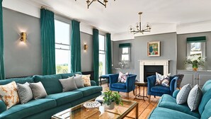 A living room with teal sofas, a glass coffee table, and a fireplace. - Chequer -  a holiday let that sleeps 14 guests  in 7 bedrooms (Rye)