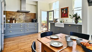 A modern kitchen with grey cabinets, a wooden dining table, and a view of the outdoors. - Chequer -  a holiday let that sleeps 14 guests  in 7 bedrooms (Rye)