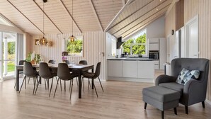 A spacious living area with a dining table, chairs, a grey armchair, and a kitchen in the background. - Nice home in Jerup with sauna (Jerup)