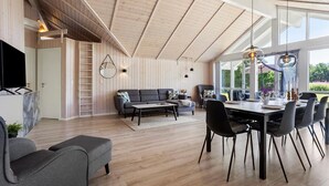 A spacious living area with a high ceiling, wooden beams, a sofa, a dining table with chairs, and a TV on a cabinet. - Nice home in Jerup with sauna (Jerup)