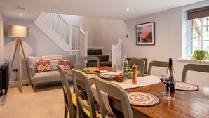 A dining area with a wooden table set for four, surrounded by chairs. A staircase with white railings leads to an upper level. - Paddock View -  a cottage that sleeps 8 guests  in 4 bedrooms (Osmotherley)