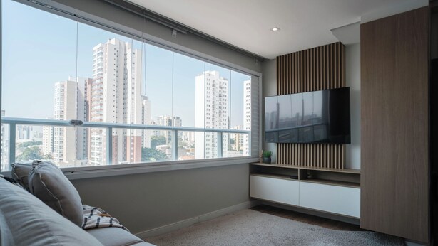Una sala moderna con un ventanal grande, un televisor de pantalla plana, un sofá y un mueble de madera.