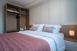 Ein Hotelzimmer mit einem Bett, einem Nachttisch mit Lampe, einem Holzschrank und einem Hängehandtuchhalter.