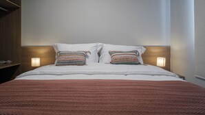 Una cama bien tendida con una colcha estampada y dos almohadones decorativos, con lámparas de pared a cada lado.