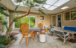 A sunlit patio with wicker furniture, a palm tree, and a view of greenery. - 3 bedroom lovely home in Nykøbing M (Nykøbing M)