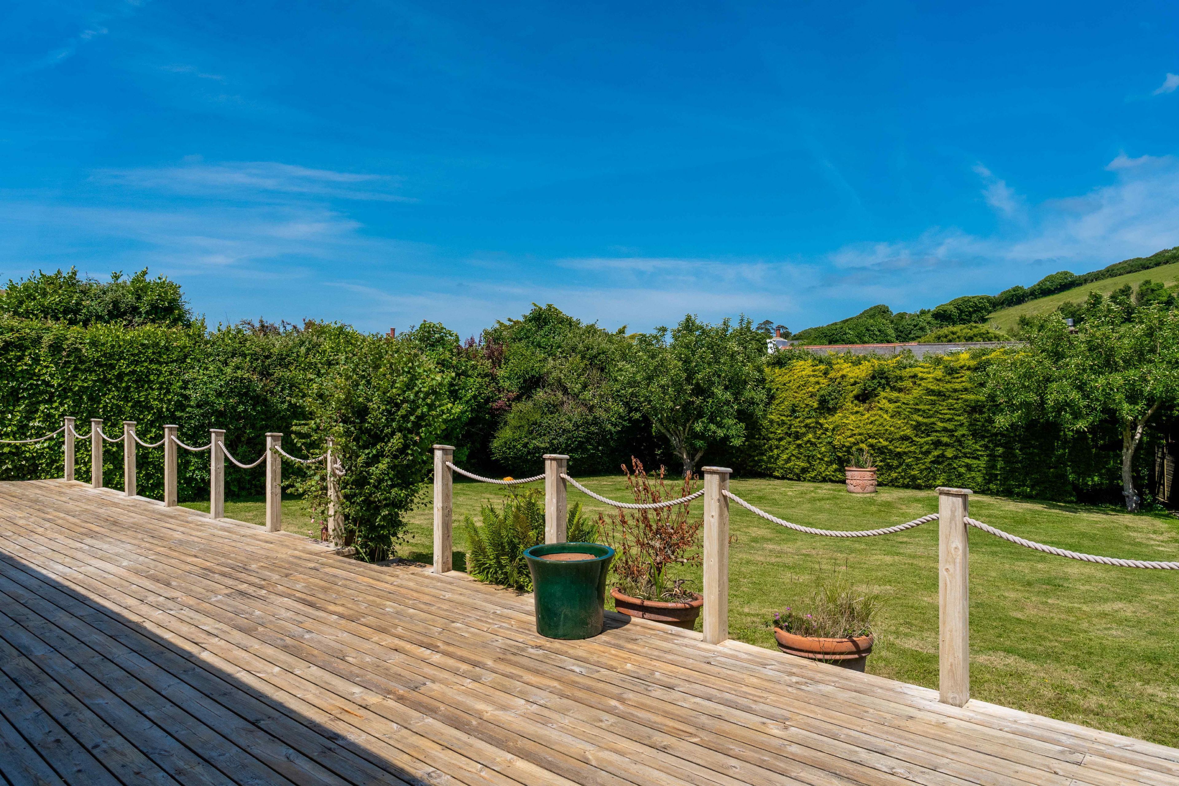 A wooden deck with a rope barrier, surrounded by lush greenery and a clear blue sky.
