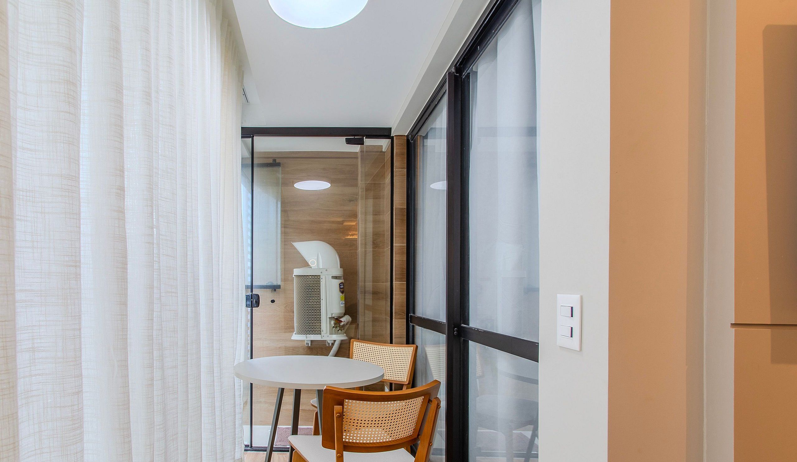 A narrow room with a glass partition, a white table, and a wooden chair.