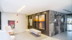 A modern lobby with a bench, seating area, and a large wall-mounted artwork depicting a sunset over water.
