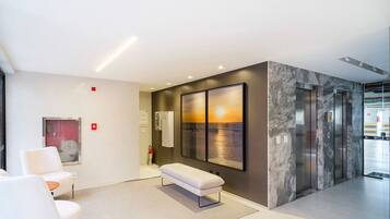 A modern lobby with a bench, seating area, and a large wall-mounted artwork depicting a sunset over water.
