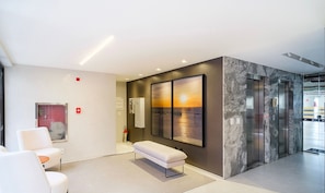 Un vestíbulo moderno con un banco, zona de estar y una gran obra de arte en la pared que representa un atardecer sobre el agua.