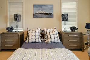 A bedroom with a bed, two nightstands, a painting of a boat, and two lamps.