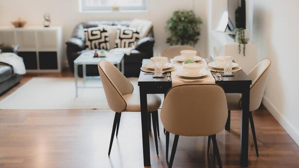 Un comedor con una mesa preparada para cuatro personas, un sofá, una mesita de centro y un televisor al fondo.