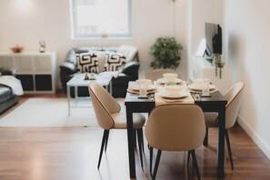 A dining area with a table set for four, a sofa, a coffee table, and a TV in the background. - City Centre Oasis - 2 Bed Apartment (Newcastle-upon-Tyne)