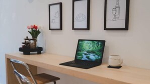 Una computadora portátil sobre un escritorio de madera, con un atril, una taza y un florero con flores.