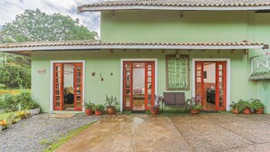 A two-story building with a tiled roof, green walls, and multiple doors. There are potted plants around the entrance and a bench in front. - Beautiful Studios in Campos do Jordao - VAE (Campos do Jordão)
