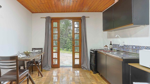 A kitchen with a wooden ceiling, a dining area with a table and chairs, and a view through a glass door to the outdoors. - Beautiful Studios in Campos do Jordao - VAE (Campos do Jordão)