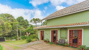 A two-story house with a tiled roof, green walls, and red-framed windows. - Beautiful Studios in Campos do Jordao - VAE (Campos do Jordão)