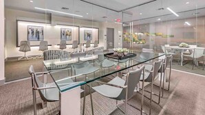 A modern conference room with glass tables and chairs, framed artwork on the walls, and a carpeted floor.