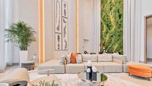 A modern living room with a sectional sofa, a glass coffee table, and a large green wall.