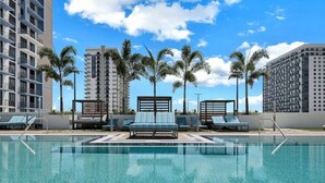 A swimming pool with lounge chairs and palm trees, surrounded by high-rise buildings.