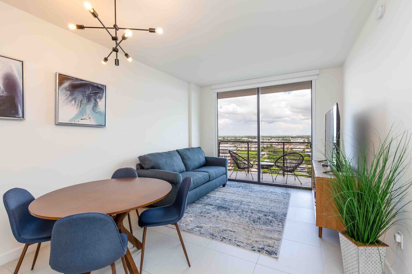 Ein modernes Wohnzimmer mit einer Couch, einem Esstisch, Stühlen, einem Fernseher und einem Balkon mit Blick.