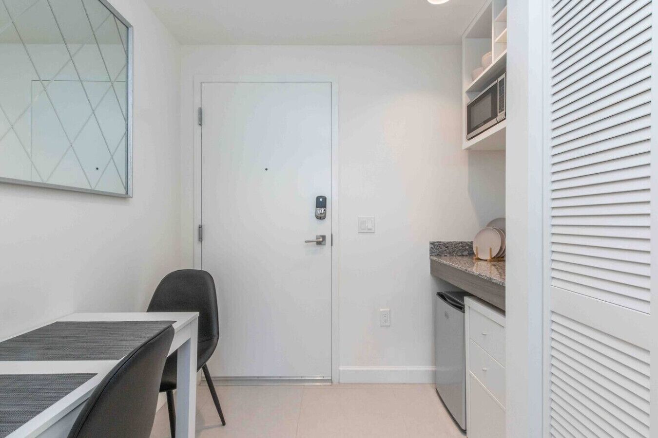 A compact kitchenette with a white door, a small dining table with chairs, and a microwave on the countertop.