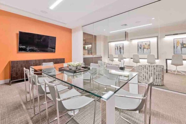 A modern conference room with glass tables and chairs, a large flat-screen TV on the wall, and artwork on the walls.