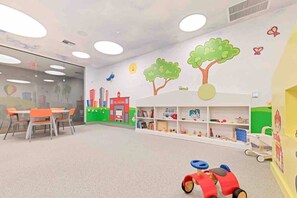 Un cuarto de juegos infantil con una mesa, sillas, una estantería y un coche de juguete.