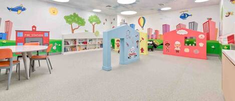 Zona de juegos infantiles con murales coloridos, un parque de bomberos y una panadería.