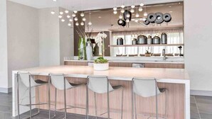 A modern kitchen with a central island, bar stools, hanging pendant lights, and kitchenware on shelves. - Modern 1BR Downtown Doral | Walk to Shops & Dining (Doral)
