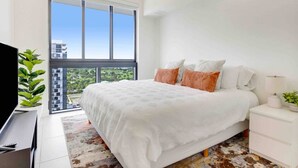 A modern bedroom with a large bed, white bedding, and a view of a cityscape through large windows. - Stylish and Modern 1BR  | Resort-Style Amenities (Doral)