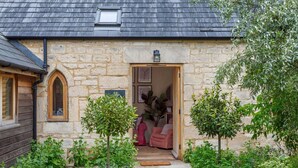 A stone building with a wooden door, a small window, and a lantern above the door. - Lemon Tree Cottage - Luxury Cottages (Painswick)