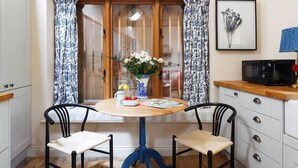 A dining area with a round table, two chairs, a vase with flowers, a microwave, and a framed picture on the wall. - Lemon Tree Cottage - Luxury Cottages (Painswick)
