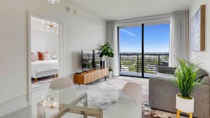 Una sala de estar moderna con un balcón, televisor, comedor y sofá.