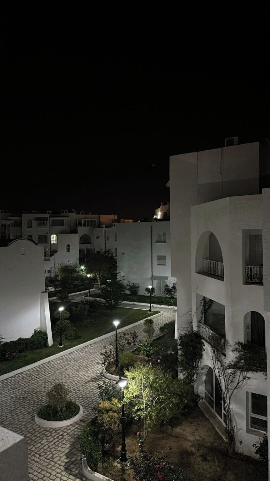 A nighttime view of a residential area with white buildings, paved pathways, and street lamps.