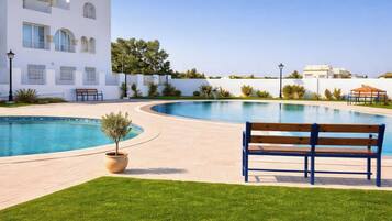 A pool area with a bench, a potted plant, and a building in the background.