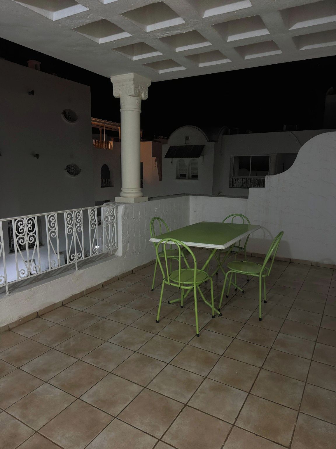 Une terrasse extérieure avec une table et des chaises, une balustrade blanche et un sol carrelé.