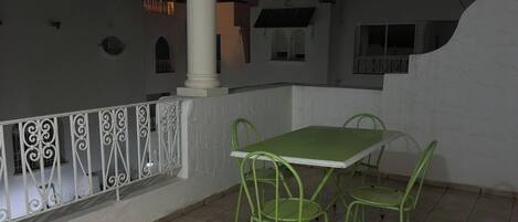 Une terrasse extérieure avec une table et des chaises, une balustrade blanche et un sol carrelé.