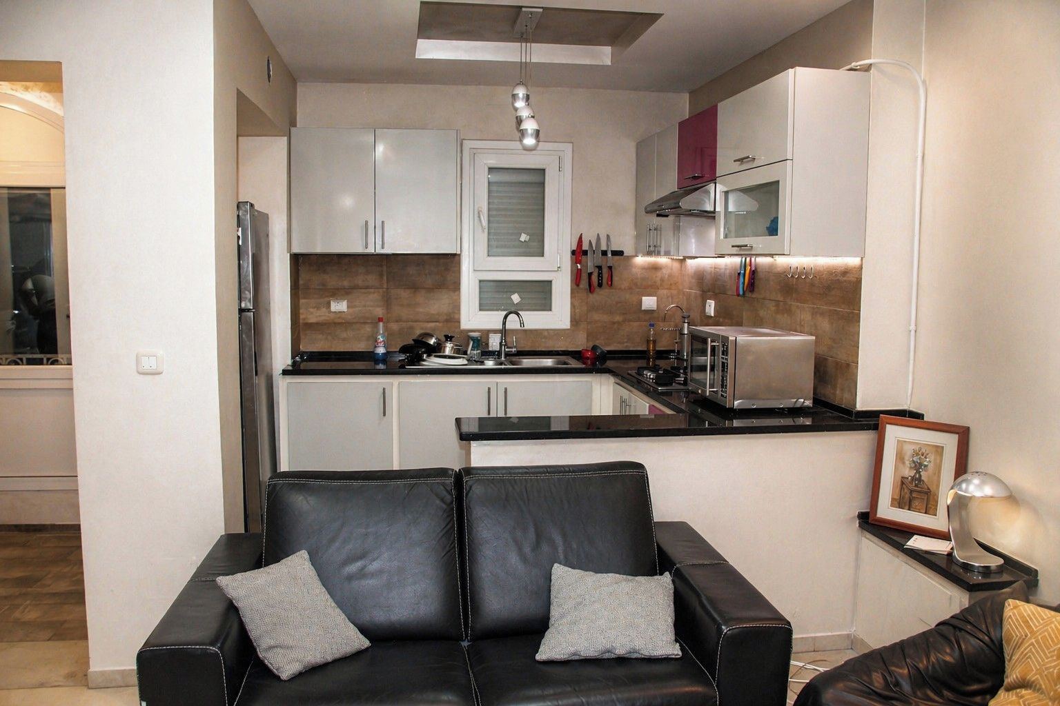 A modern kitchen with white cabinets, a black countertop, and a stainless steel refrigerator.